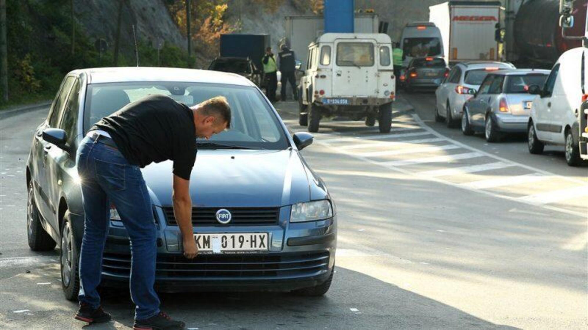 Un automobilista toglie gli adesivi messi per coprire i riferimenti serbi sulla sua targa