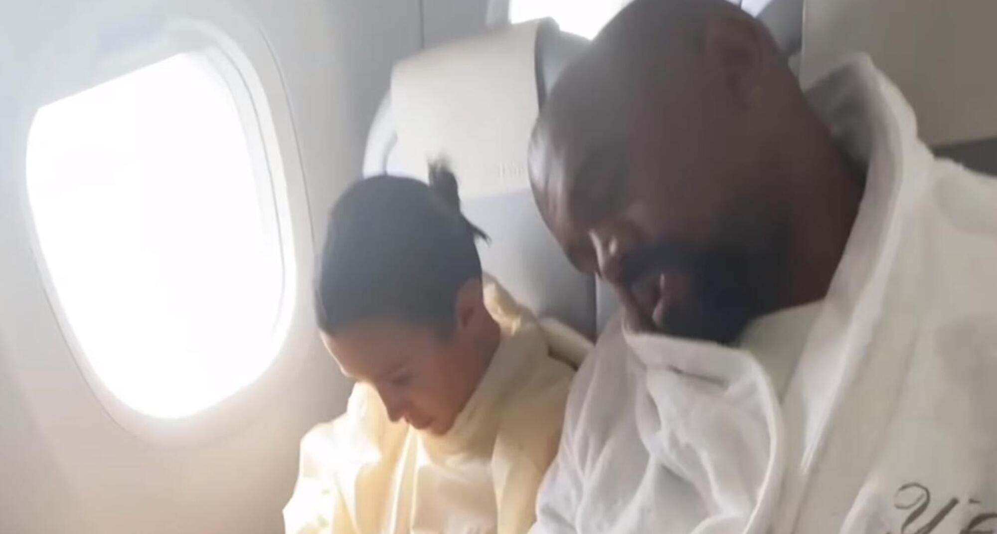 Bianca Censori (col telefono) e Kanye West (appisolato) sul volo in economy